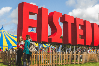 Photo showing the eisteddfod site on a bright day with clear blue skies. The huge eisteddfod letters are in he foreground with the main pavillion in the background.