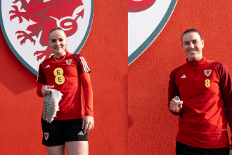 Wales Women players, Lily Woodham and Gemma Evans standing in front ofa red background withe FAW dragon logo on it, holidng the boots and the tooth they have donated to the museum.